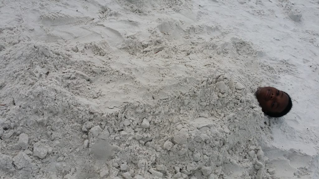 A black boy laying in the sand, buried.